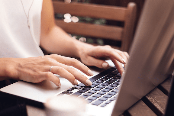 Closeup of a woman's hands typing at laptop while outside on a porch.